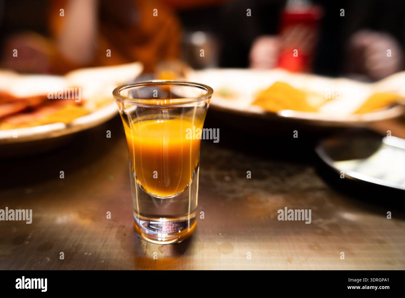 Bicchiere da pub irlandese con liquido ambrato su un tavolo in legno, piastre di sfondo per alimenti, illuminazione ambiente calda Foto Stock