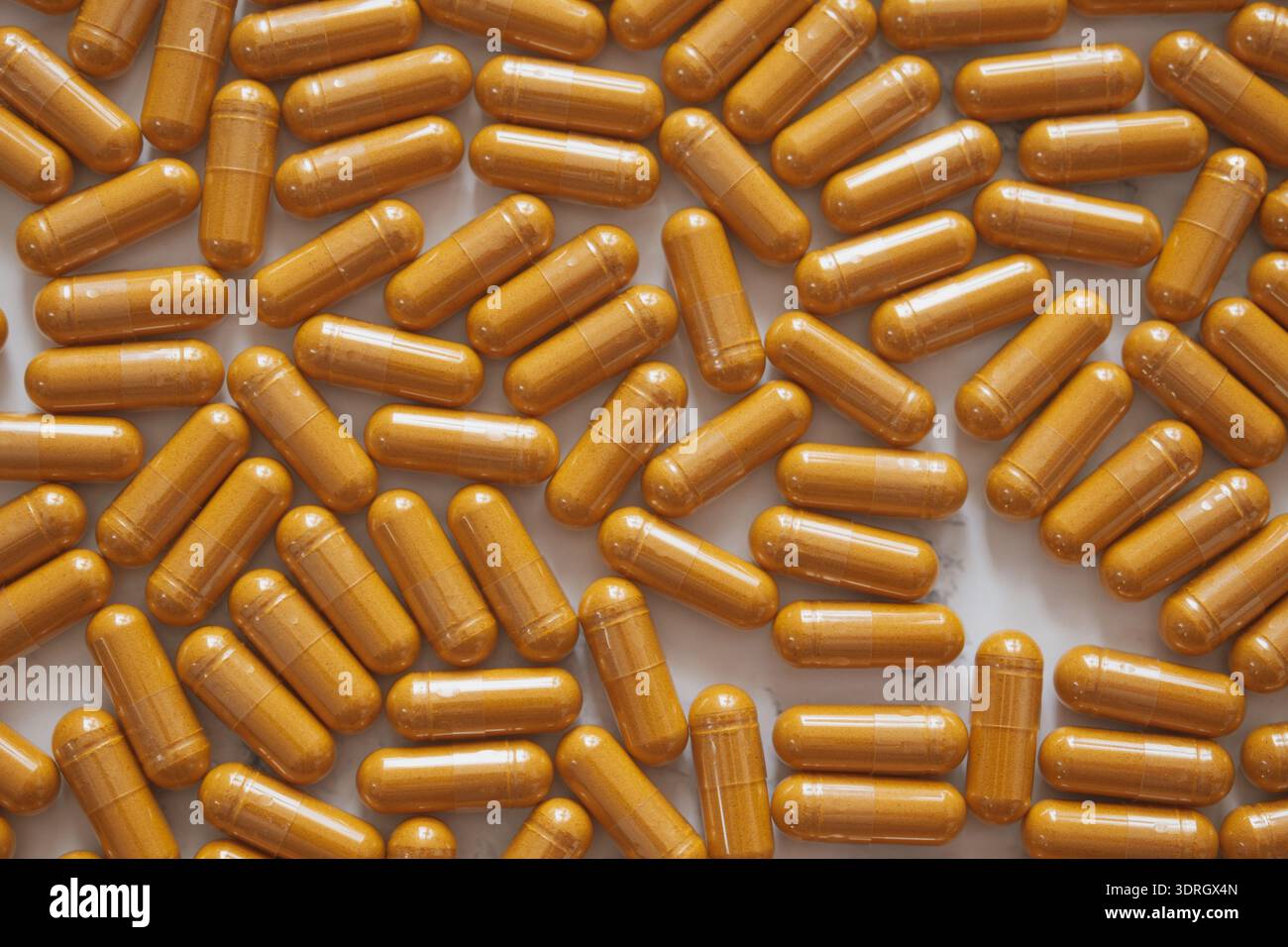 Piatto dall'alto minimalista con capsule luminose di curcumina sparse su marmo bianco, che mettono in risalto l'estetica vibrante del benessere e lo stile pulito e moderno Foto Stock