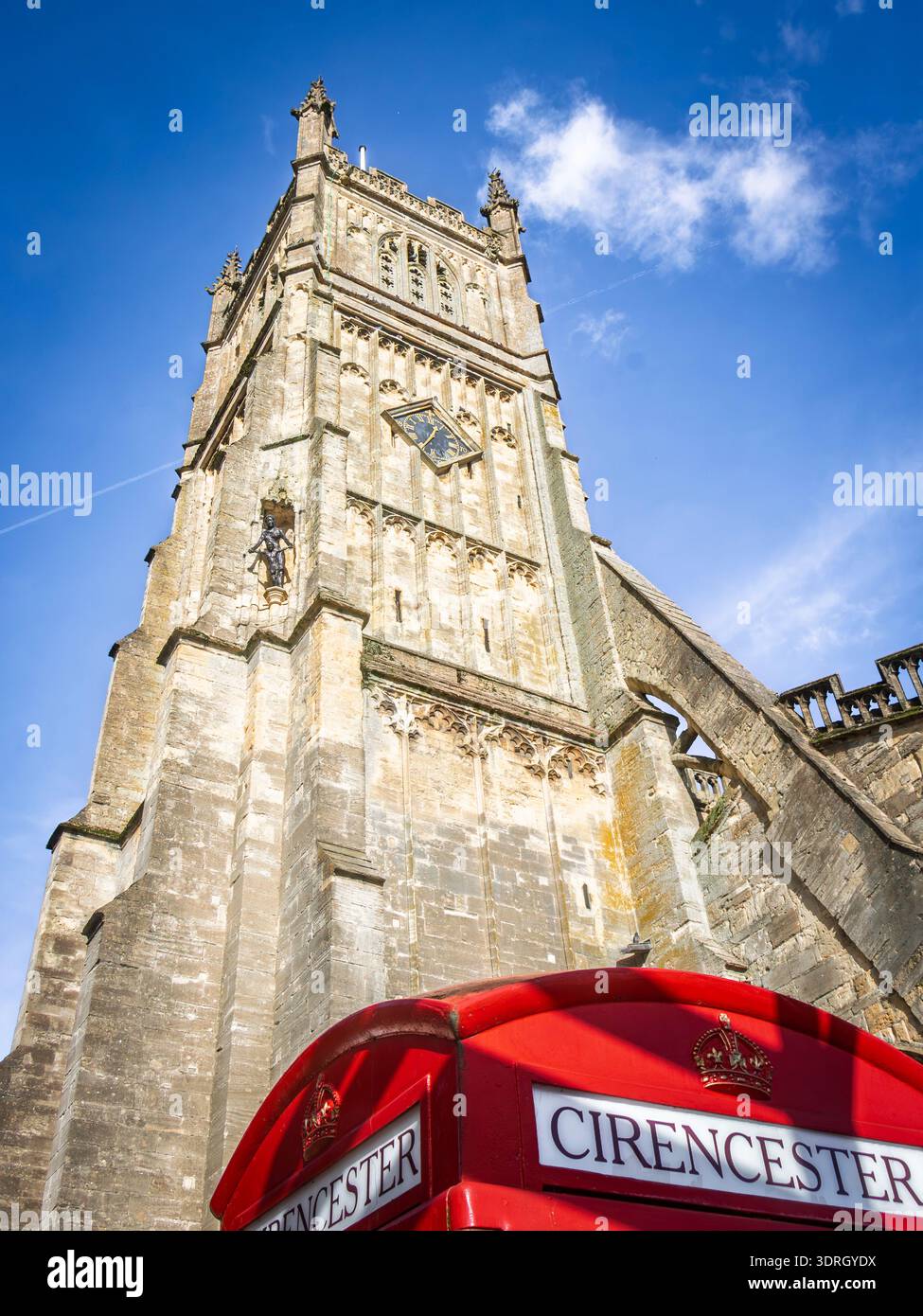 Vista ad angolo basso di una storica torre abbaziale in pietra di cirencester e di una classica cabina telefonica rossa vibrante a Cirencester Foto Stock