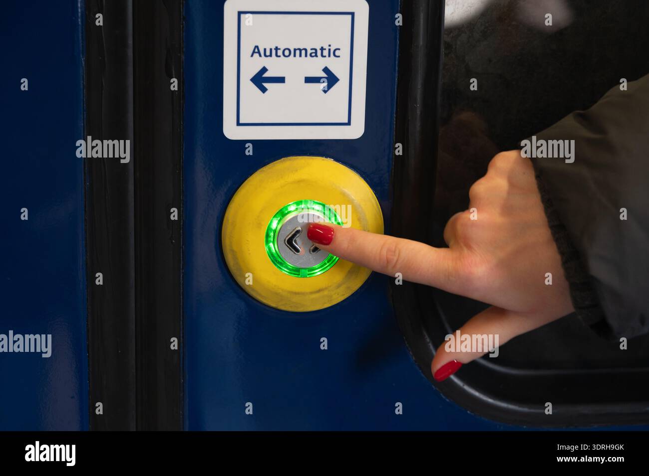 Pulsante porta automatico a pressione manuale femmina, anello illuminato verde e cornice gialla, chiodi lucidati rossi, maniche invernali, primo piano dei trasporti pubblici Foto Stock