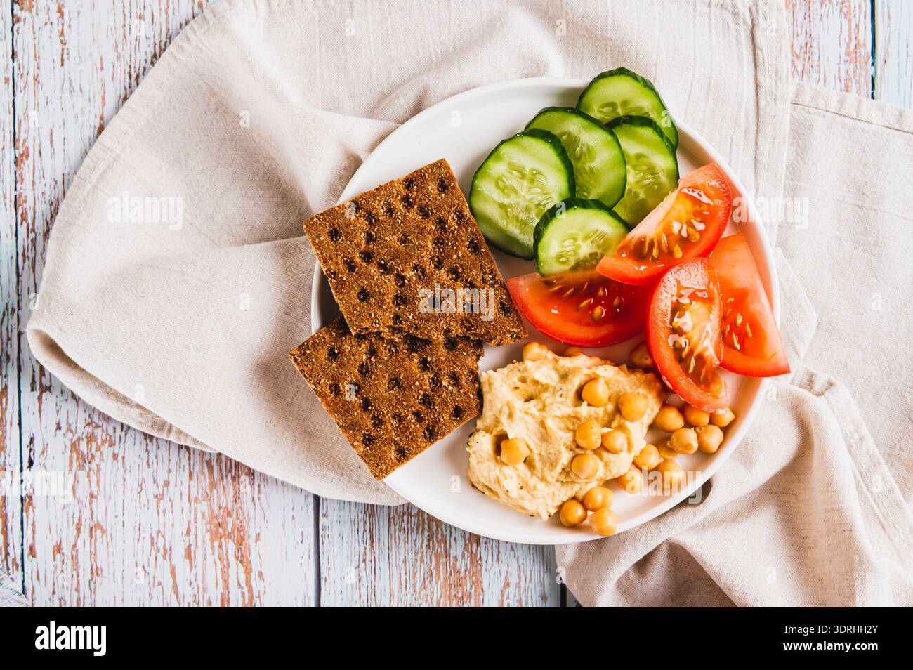 Primo piano di platte con hummus, ceci, pomodoro, cetriolo e cracker di grano su una vista dall'alto del piatto Foto Stock