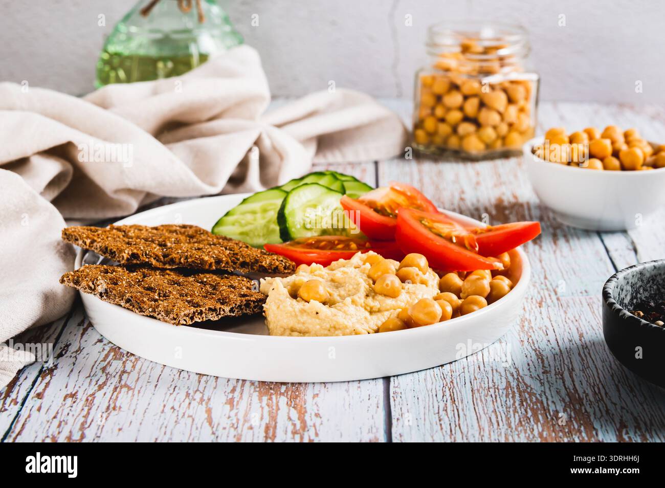 Hummus, ceci, pomodoro, cetriolo, cracker di grano su un piatto sul tavolo Foto Stock