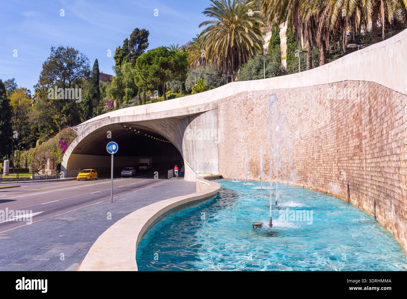 Infrastruttura urbana moderna con tunnel e fontana che mostrano un ingresso stradale accanto a un elemento d'acqua decorativo con spruzzi verticali e tropicali Foto Stock