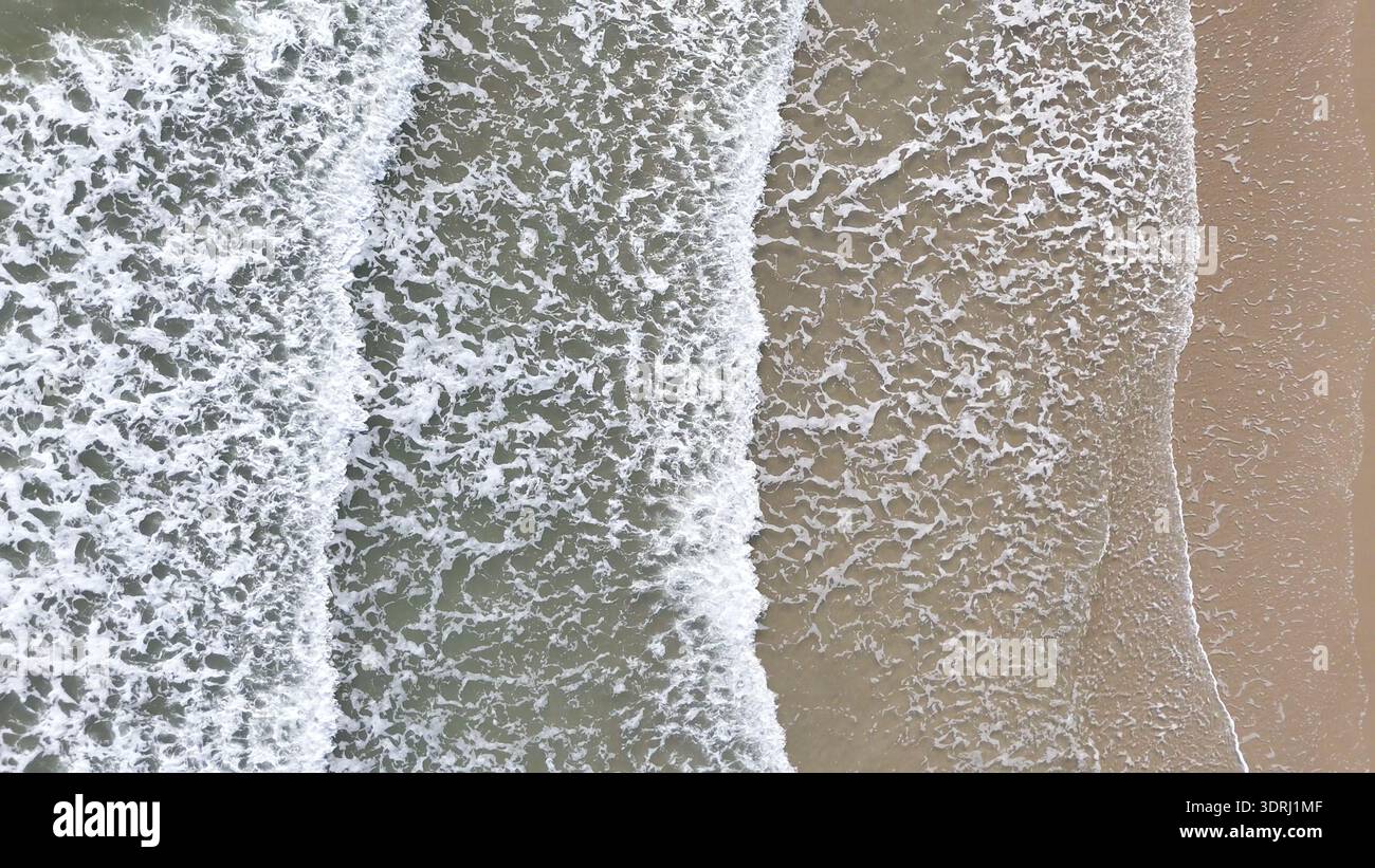 Vista aerea delle dolci onde dell'oceano che si stagliano su una spiaggia sabbiosa Foto Stock