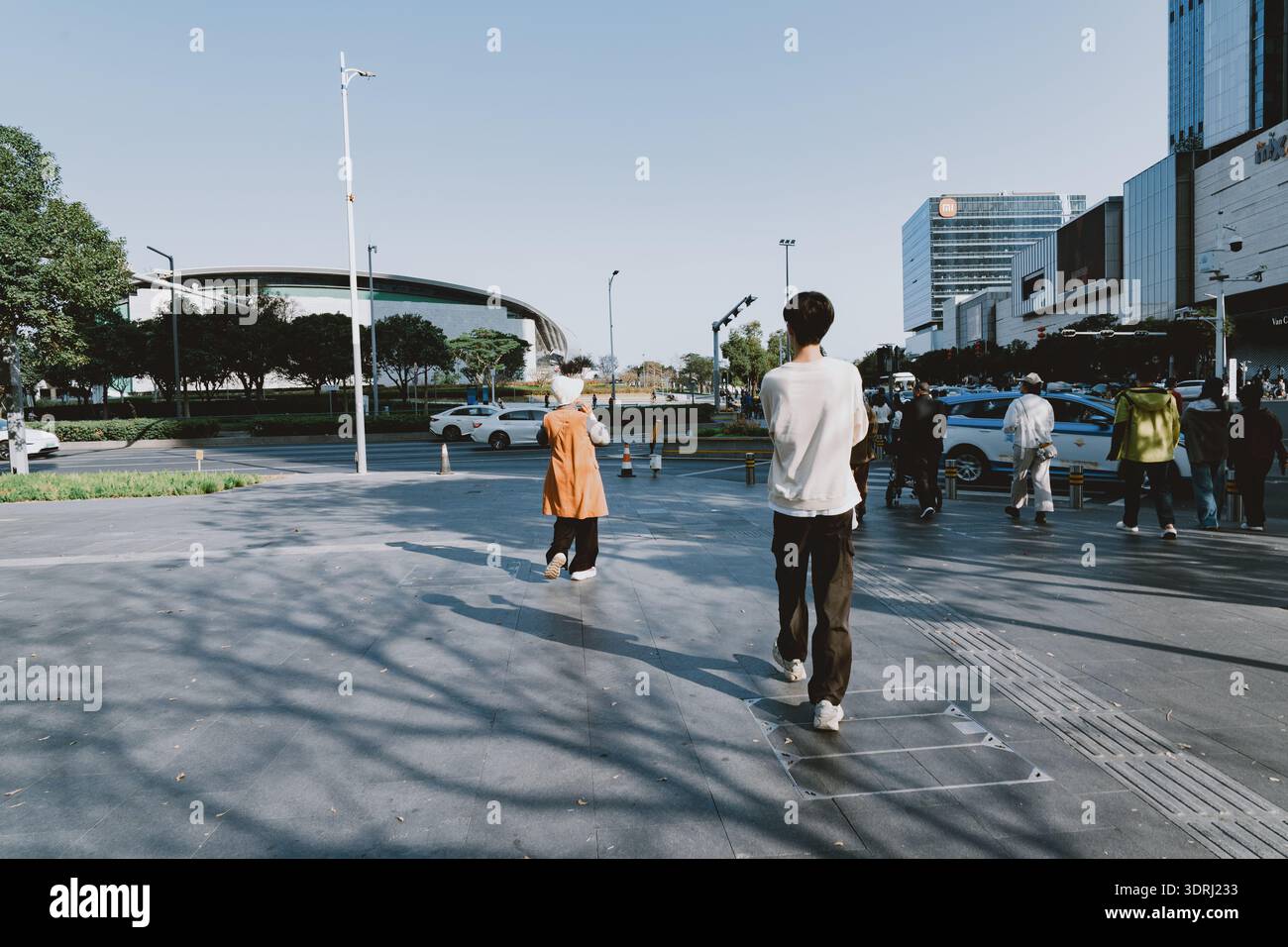Persone che camminano per le strade urbane della città moderna sotto il cielo limpido con ombre gettate sul marciapiede Foto Stock