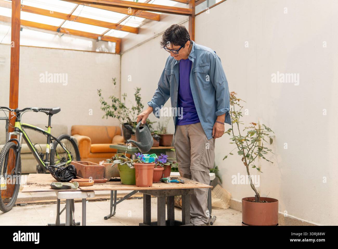 La persona sta innaffiando le piante in vaso su un patio, impegnandosi in un rilassante hobby di giardinaggio Foto Stock