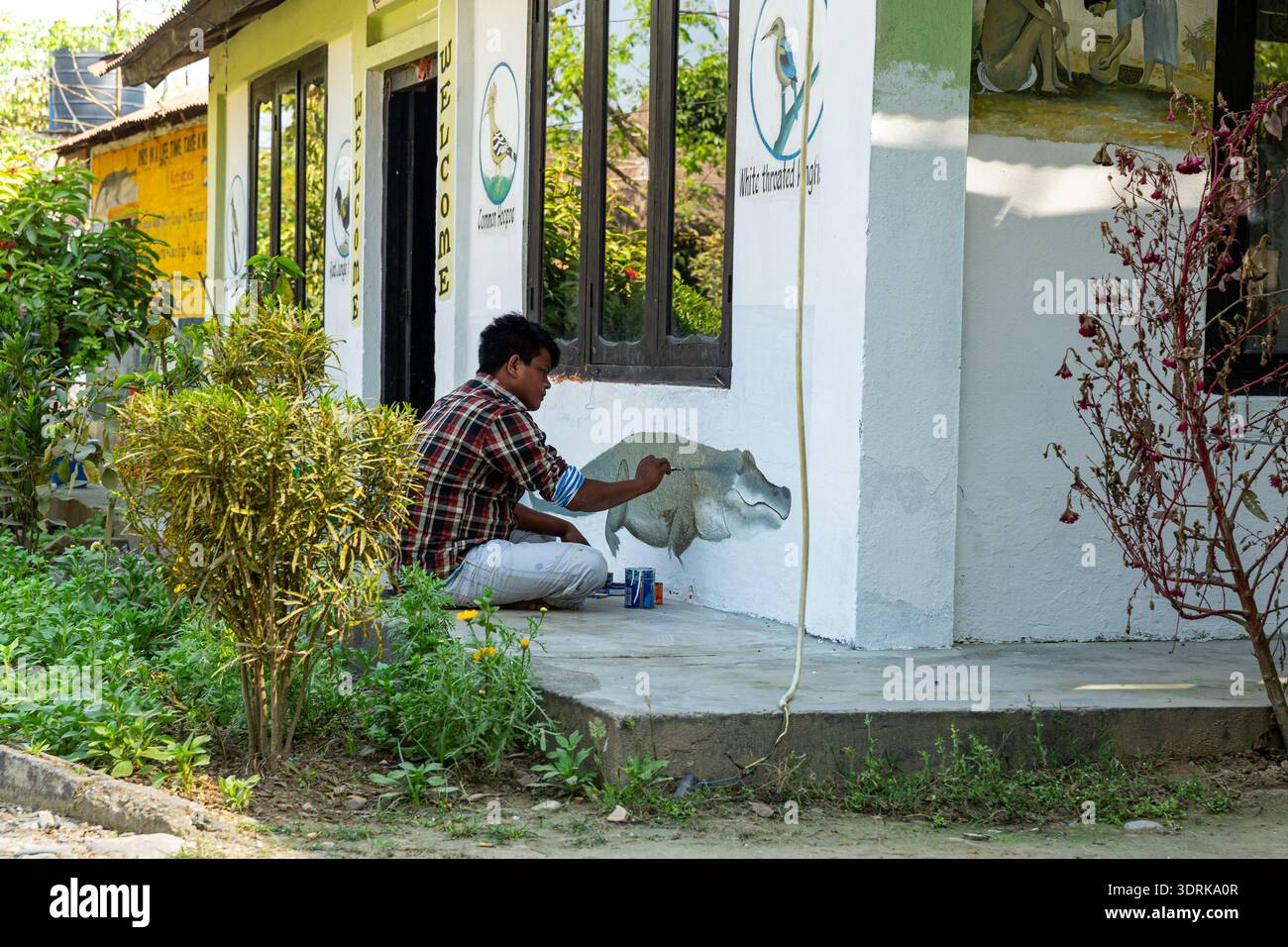 Parco nazionale di Chitwan, Nepal - 9 marzo 2015: Uomo che dipinge arte murale a tema faunistico che promuove la consapevolezza ambientale nell'area comunitaria del parco nazionale. Foto Stock