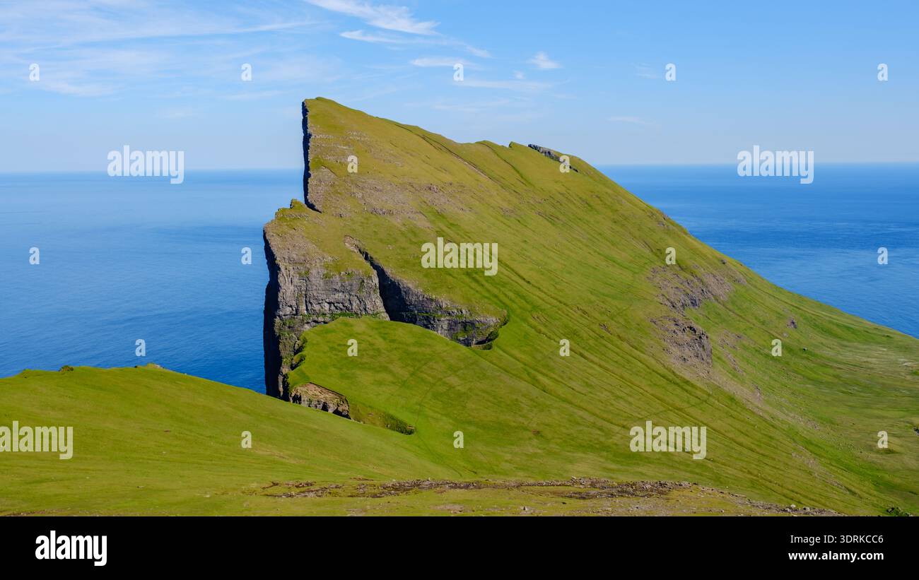 Una splendida formazione rocciosa sorge drammaticamente dal vibrante paesaggio verde, offrendo vedute mozzafiato dell'oceano sottostante. Isole Mylingur Faroe Foto Stock
