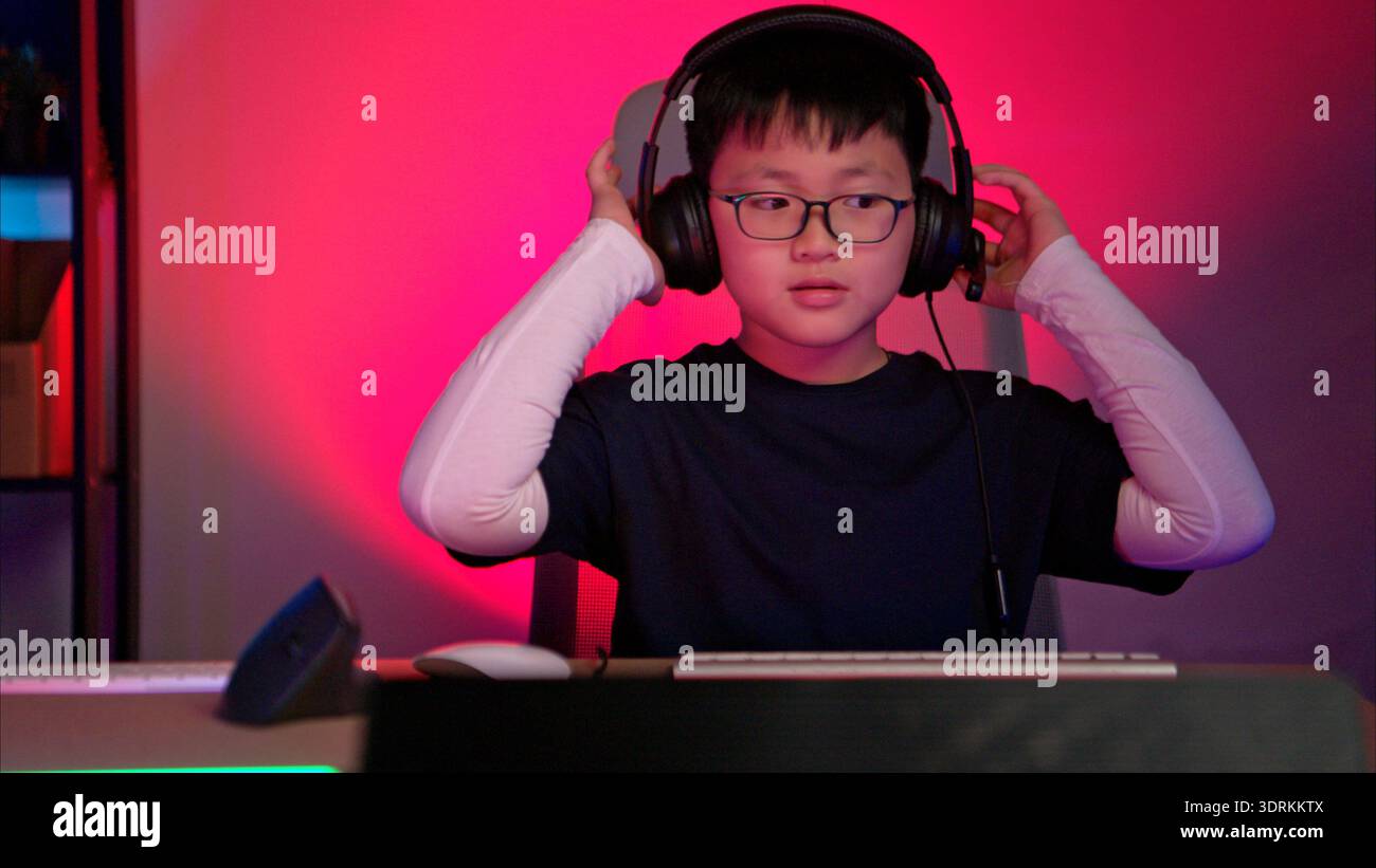 Un ragazzo che indossa le cuffie e gioca su un computer desktop in un ambiente di gioco colorato Foto Stock
