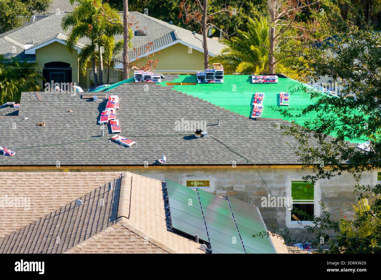 Tegole di asfalto applicate sul nuovo tetto della casa. Operai di tetti che proteggono i timpani. Cantiere residenziale in Florida. Foto Stock