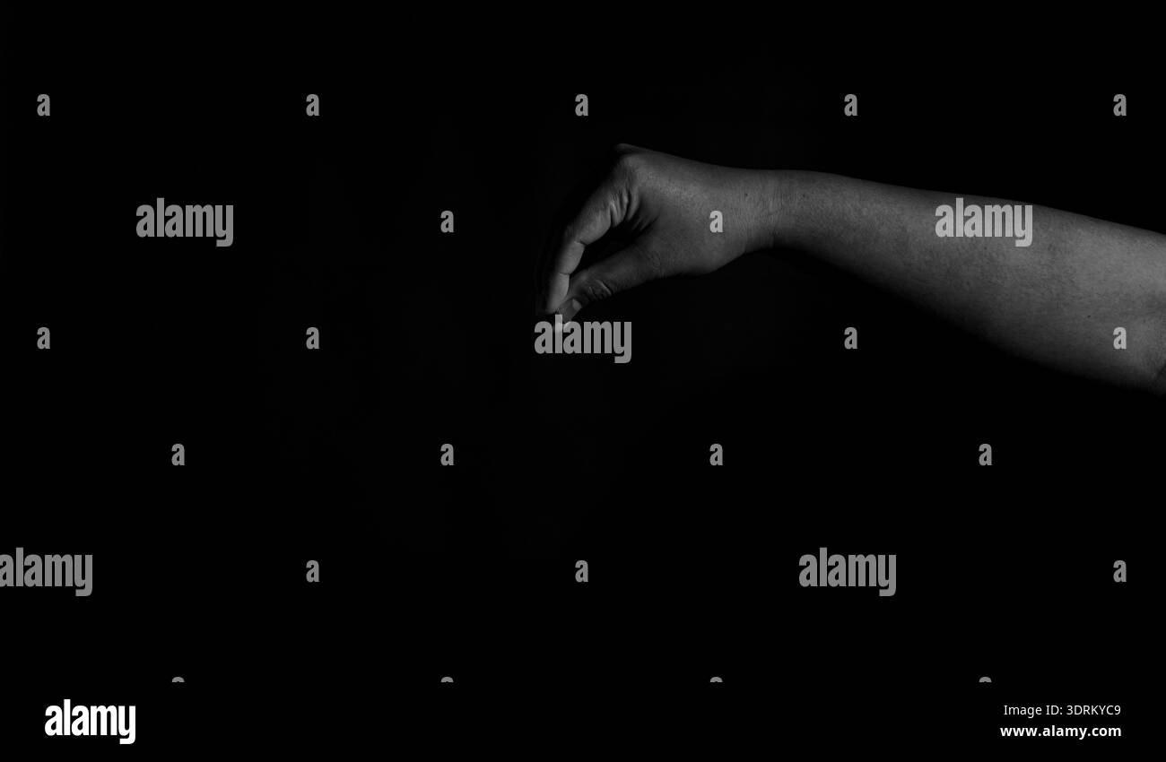 Immagine della mano in bianco e nero dai toni bassi con gesti di avvicinamento, isolata su sfondo nero con luci sottili e profondità delle ombre. Foto Stock