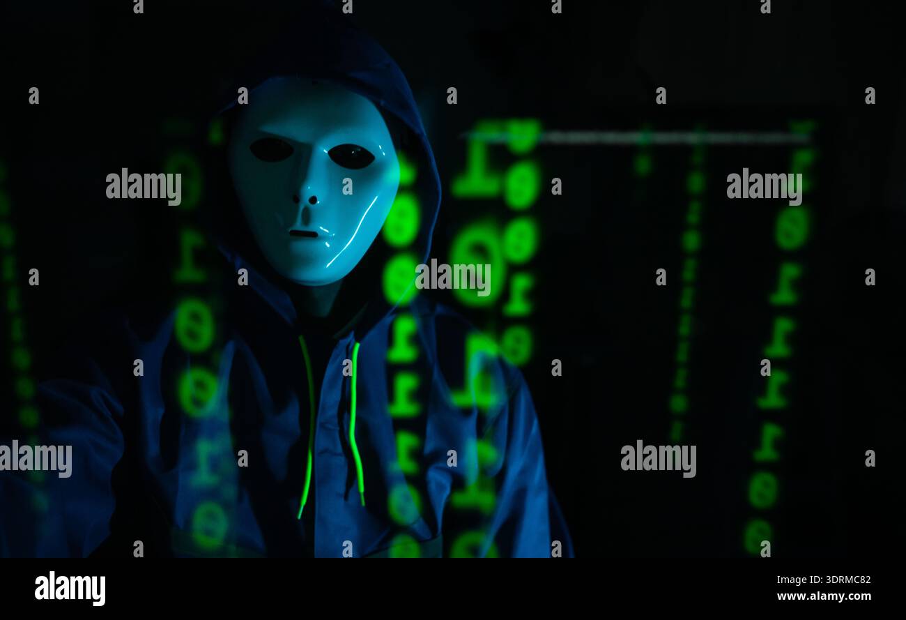 Hacker anonimo che indossa una maschera e una felpa con cappuccio che interagiscono con i dati digitali in una stanza buia, rappresentando la criminalità informatica e le minacce alla sicurezza online Foto Stock