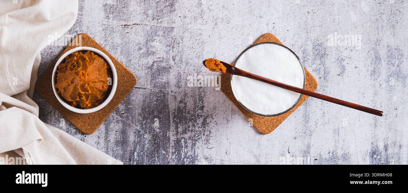 Latte con aggiunta di miso in un bicchiere e una ciotola di pasta di miso sul banner Web della vista superiore del tavolo Foto Stock