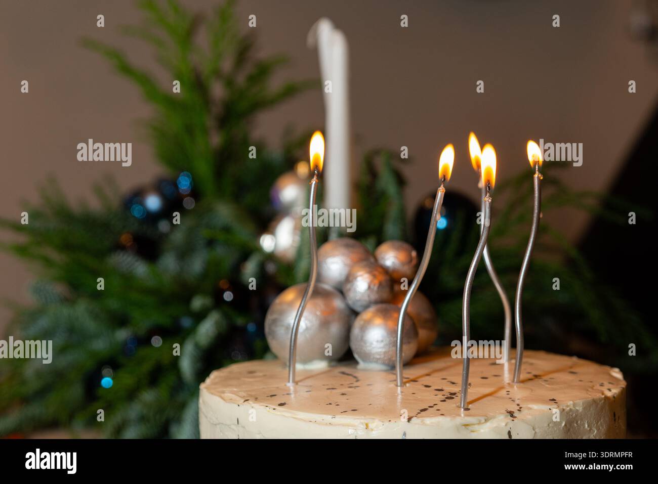 Primo piano di una torta smerigliata bianca con candele d'argento ondulato e baule in argento metallizzato, con un pezzo centrale per le vacanze sempre sfocato sul retro Foto Stock
