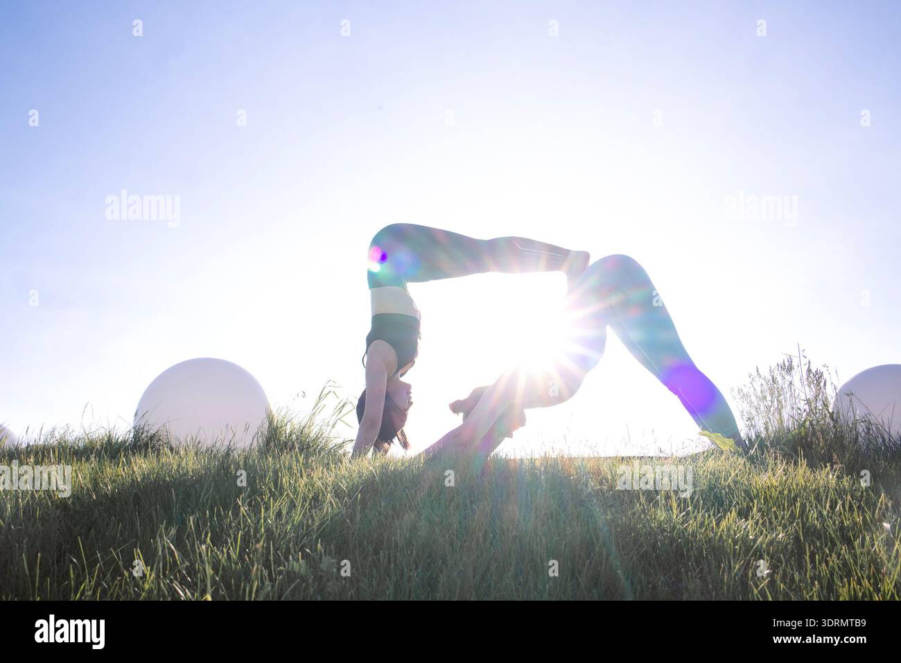 Donna flessibile che esegue lo yoga in un campo illuminato dal sole, che mostra forza ed equilibrio, con erba morbida e luce solare brillante Foto Stock