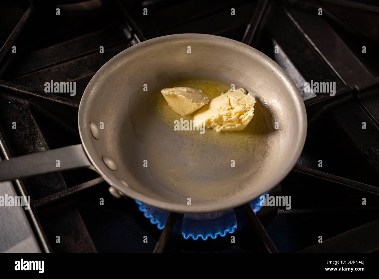 Primo piano del burro che si scioglie nella padella sul piano cottura a gas. Foto Stock