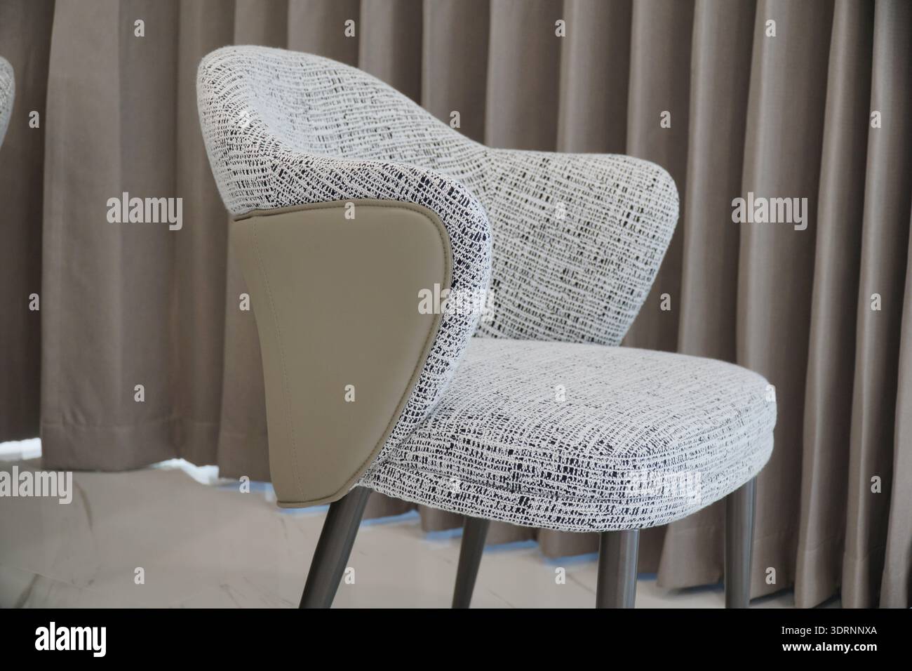 Sedia bianca con schienale marrone seduta davanti a una tenda. La sedia è realizzata in tessuto e ha un design unico. La tenda dietro Foto Stock
