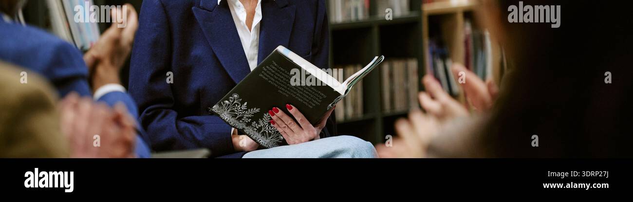 Donna di mezza età che legge il libro durante la presentazione in biblioteca Foto Stock