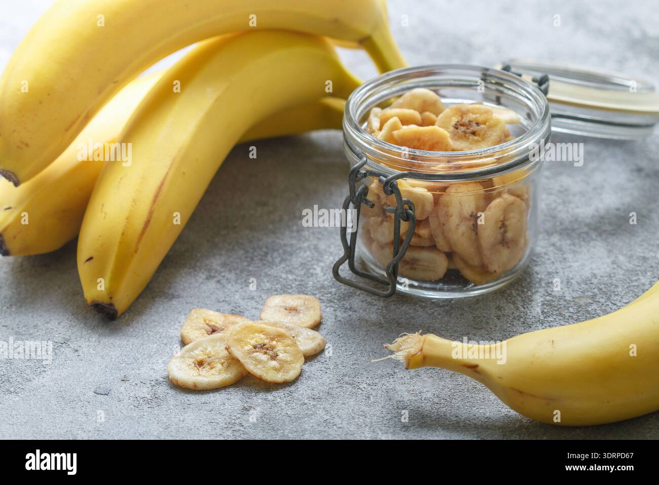 Banane secche fatte in casa in un vaso di vetro e banane fresche. Fette di frutta fritte gialle. Spuntino dolce sano. Vegetarianismo Foto Stock