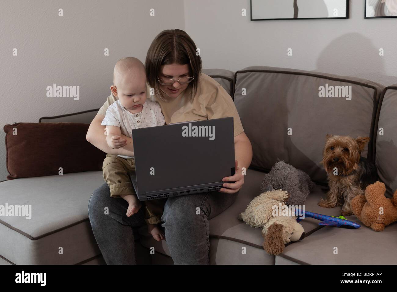 Un genitore è in grado di operare in multitasking mentre utilizza un notebook, prendersi cura del bambino e gestire gli animali domestici in un ambiente accogliente Foto Stock