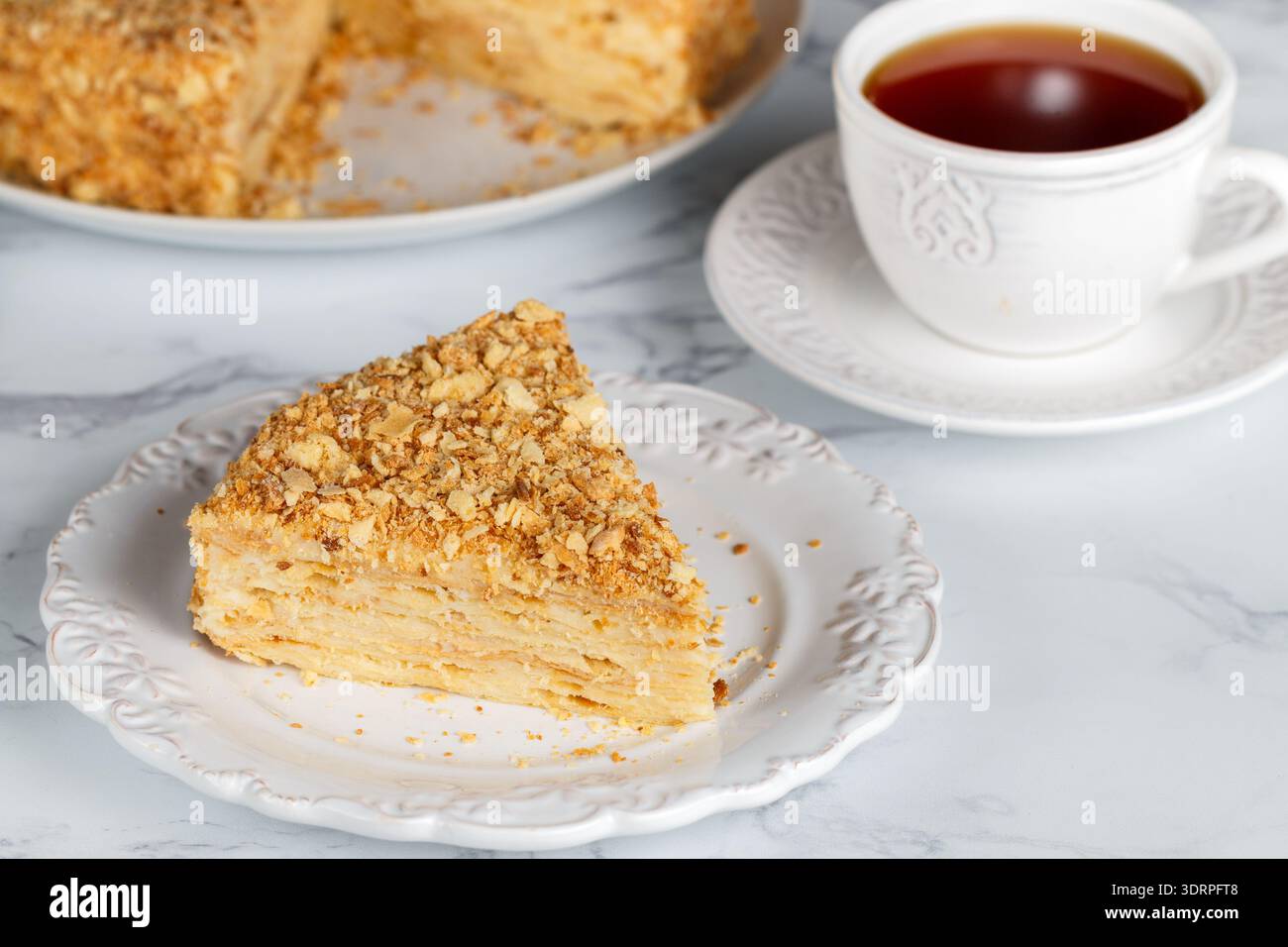 Un pezzo di torta Napoleone su un piatto bianco su un tavolo di marmo. dessert a strati. preparato con pasta sfoglia con uno strato di panna. Selez Foto Stock
