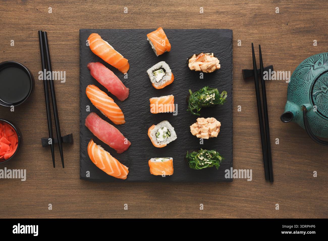 Sushi servito su un piatto nero con bastoncini e tè su un tavolo di legno Foto Stock