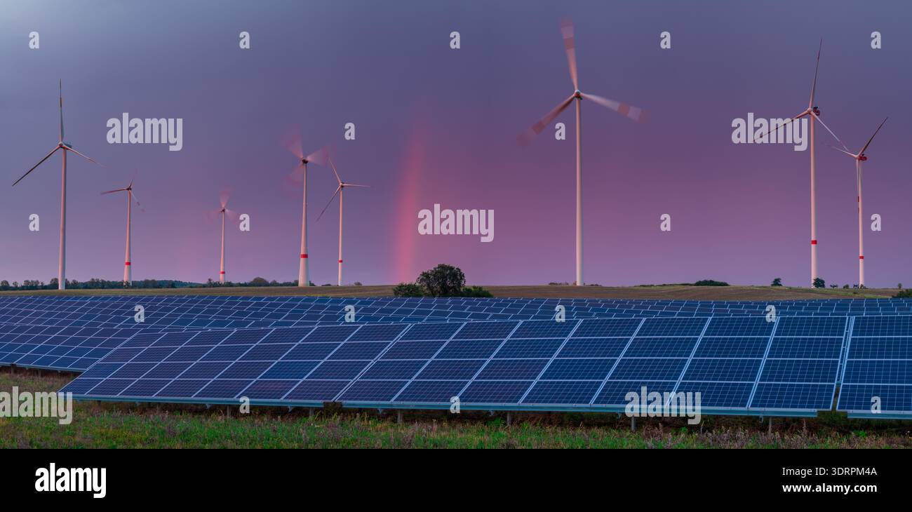 Una fattoria solare vicino a un parco eolico contro un cielo dinamico Foto Stock