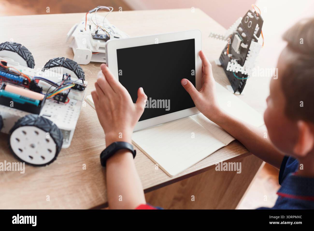 Bambino che usa il tablet per controllare l'auto robot nello spazio interno con i robot giocattolo in giro Foto Stock