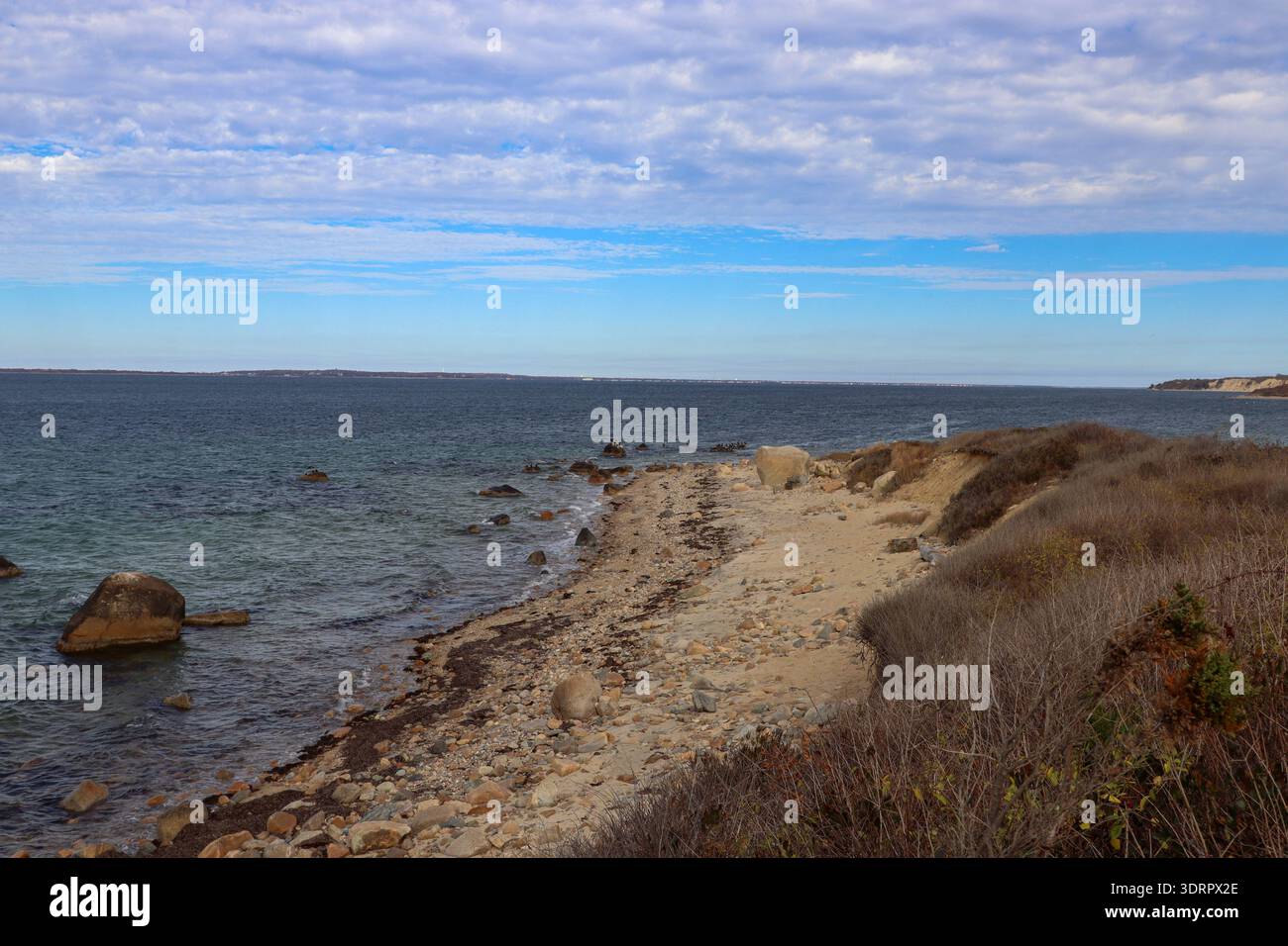 Spiaggia di sabbia ricurva con rocce sparse e mare blu calmo sotto un cielo nuvoloso e strutturato. Foto Stock