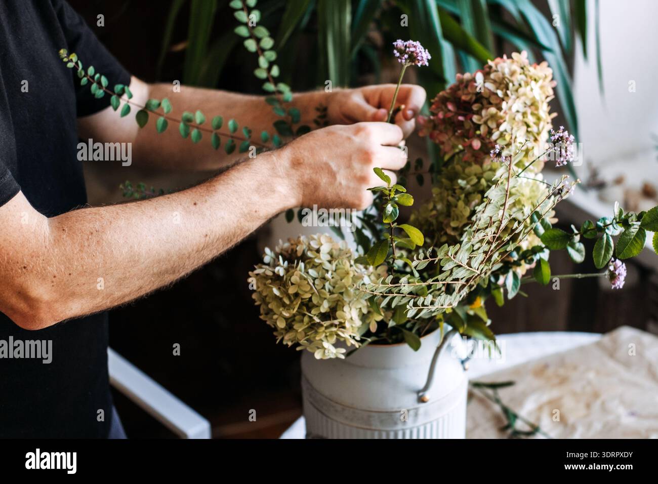 Florist organizza rami frondosi e ortensie in lattina bianca di metallo. Fiori eleganti in agriturismo, arredi rustici e floreali per la casa, vasi vintage, campagna Foto Stock