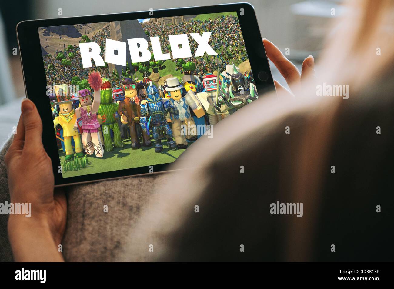 Riga, Lettonia - 2 febbraio 2026: Primo piano di un bambino che tiene un tablet e gioca a Roblox a casa. I coloratissimi personaggi di gioco sullo schermo mettono in risalto i dispositivi mobili Foto Stock