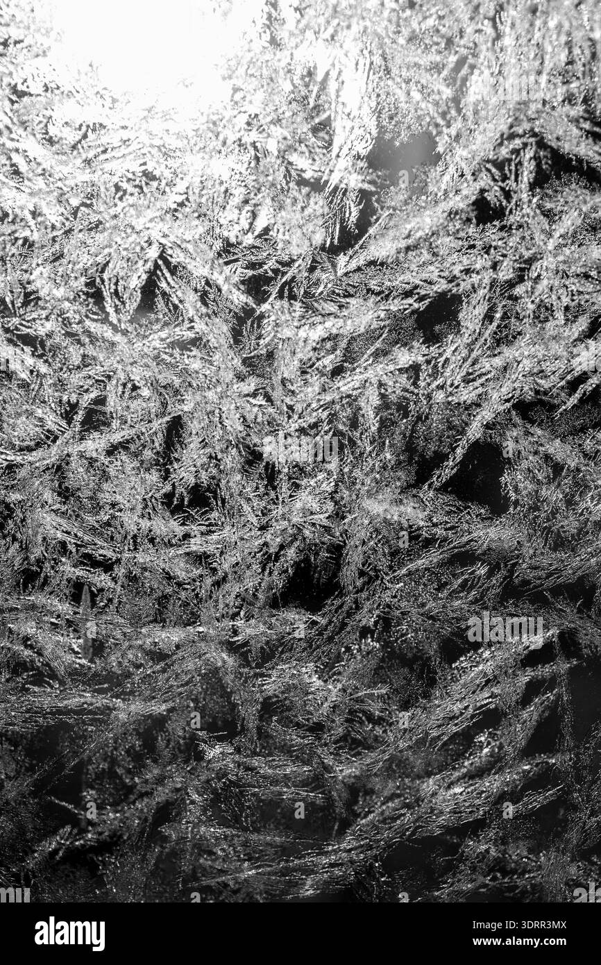 L'immagine mostra intricati motivi di gelo che formano delicate forme cristalline su una finestra. La luce soffusa mette in risalto i dettagli sfumati e crea una cal Foto Stock