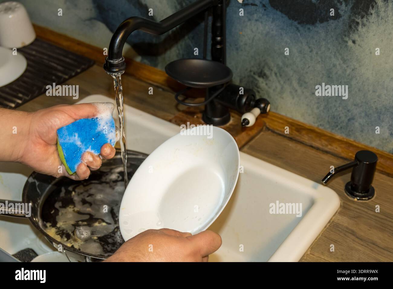 lavare i piatti con spugna e acqua corrente nel lavello della cucina Foto Stock