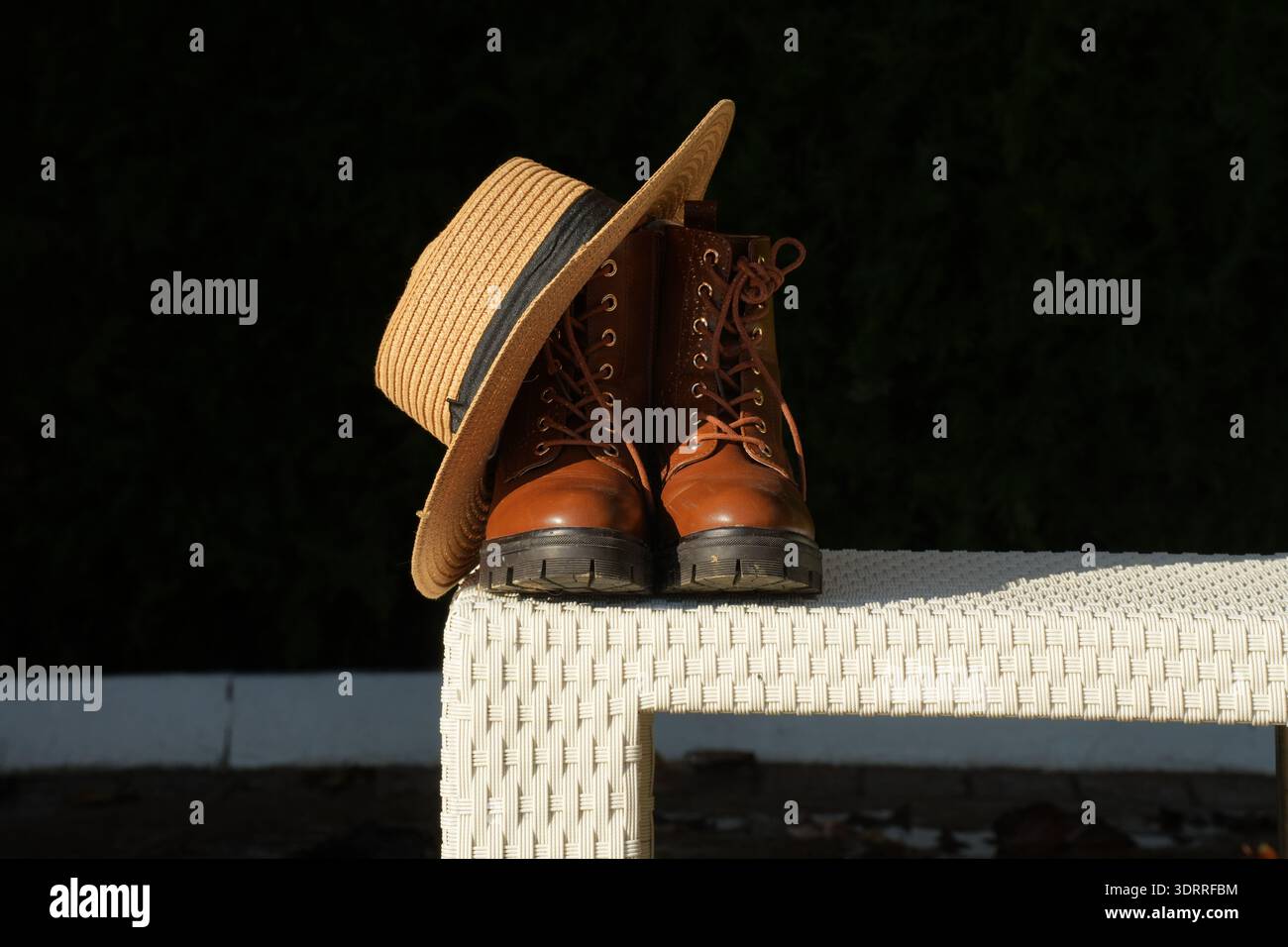 Stivali in pelle marrone con cappello di paglia alla luce del sole che simboleggiano l'estetica slow-living del cottagecore revival della moda sostenibile, viaggi consapevoli e Foto Stock