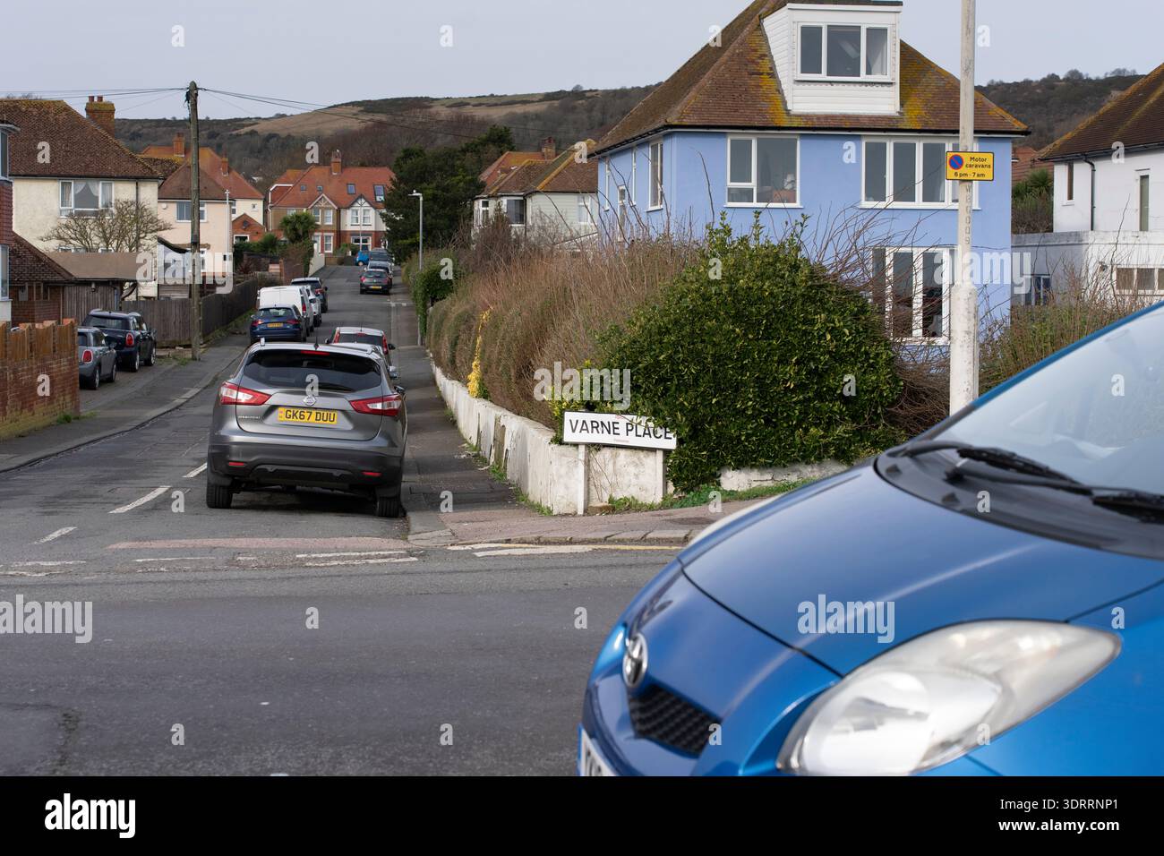 Auto parcheggiate a Varne Place, Folkestone, Kent, Regno Unito. Una strada residenziale con case e una collina sullo sfondo. Foto Stock