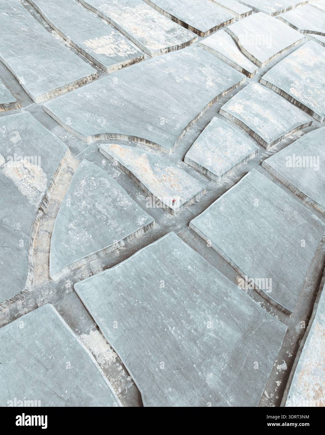 La vista aerea delle saline geometriche crea un mosaico astratto di bianchi e grigi sotto il sole siciliano, in contrasto con gli stretti sentieri della Sicilia Foto Stock