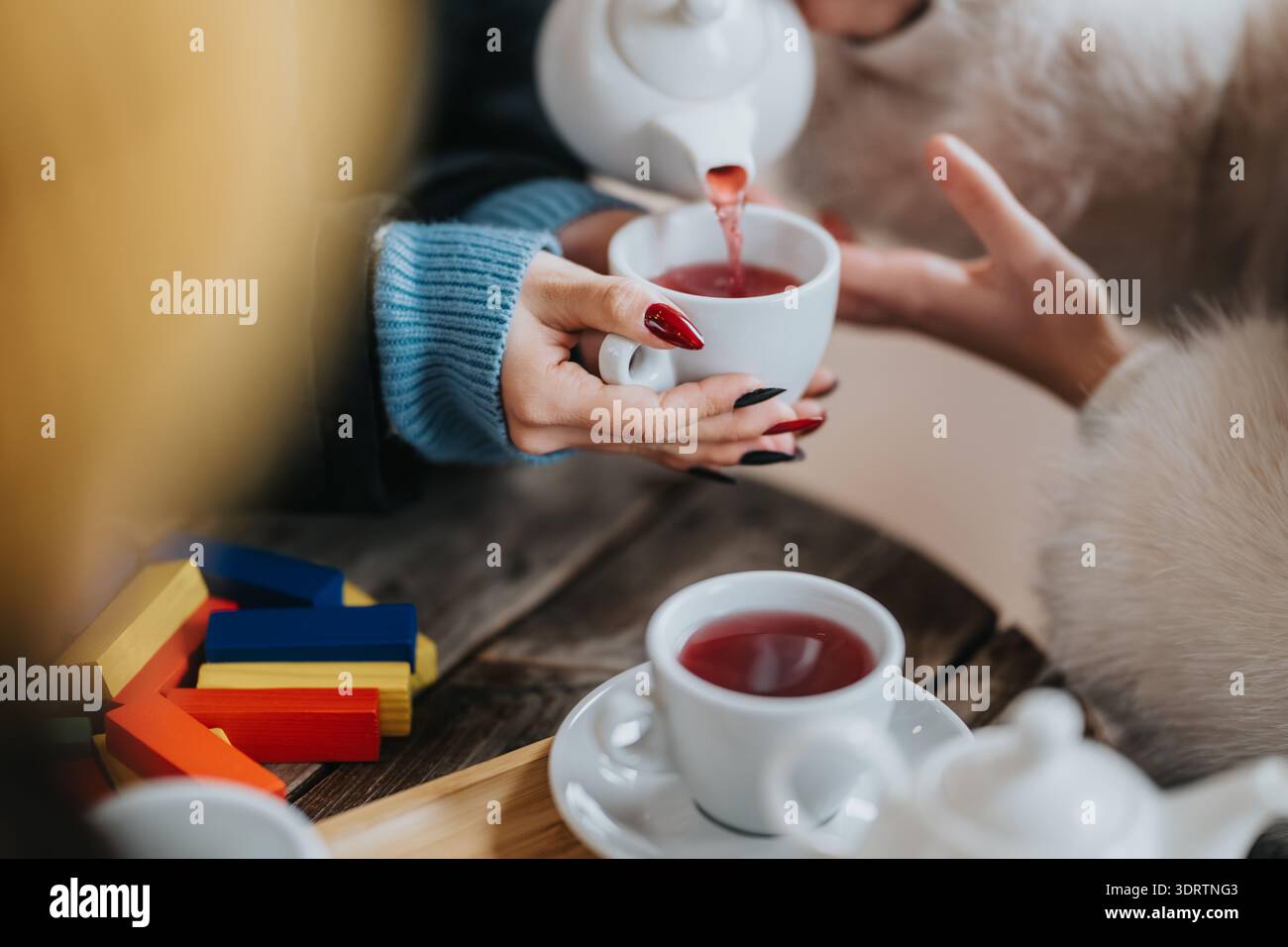 Le ragazze condividono un intimo momento di tè con tazze da tè rosse e colorati blocchi di legno su un tavolo rustico Foto Stock