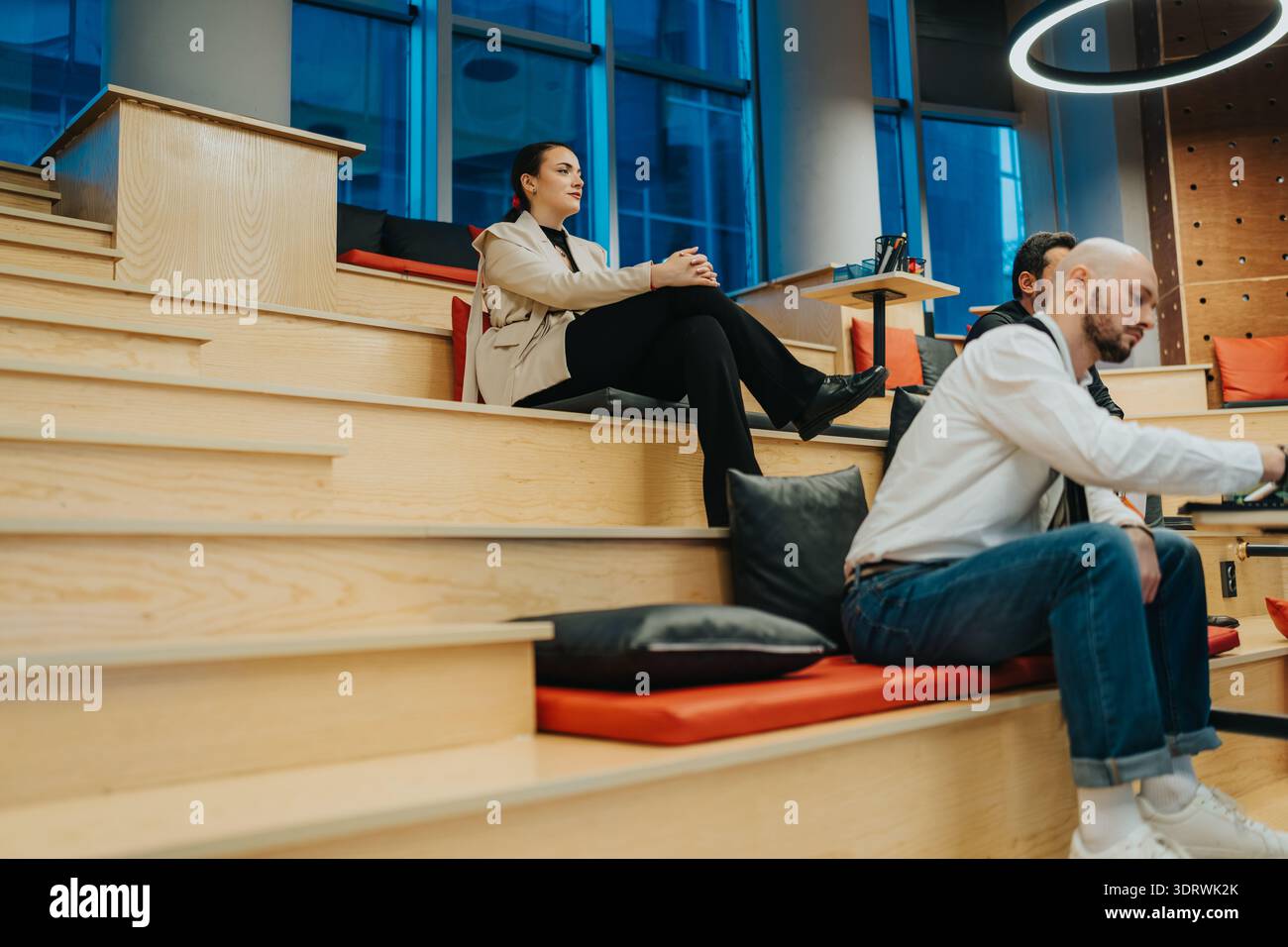 Professionisti rilassati in una moderna lounge di coworking su gradini in legno con cuscini Foto Stock