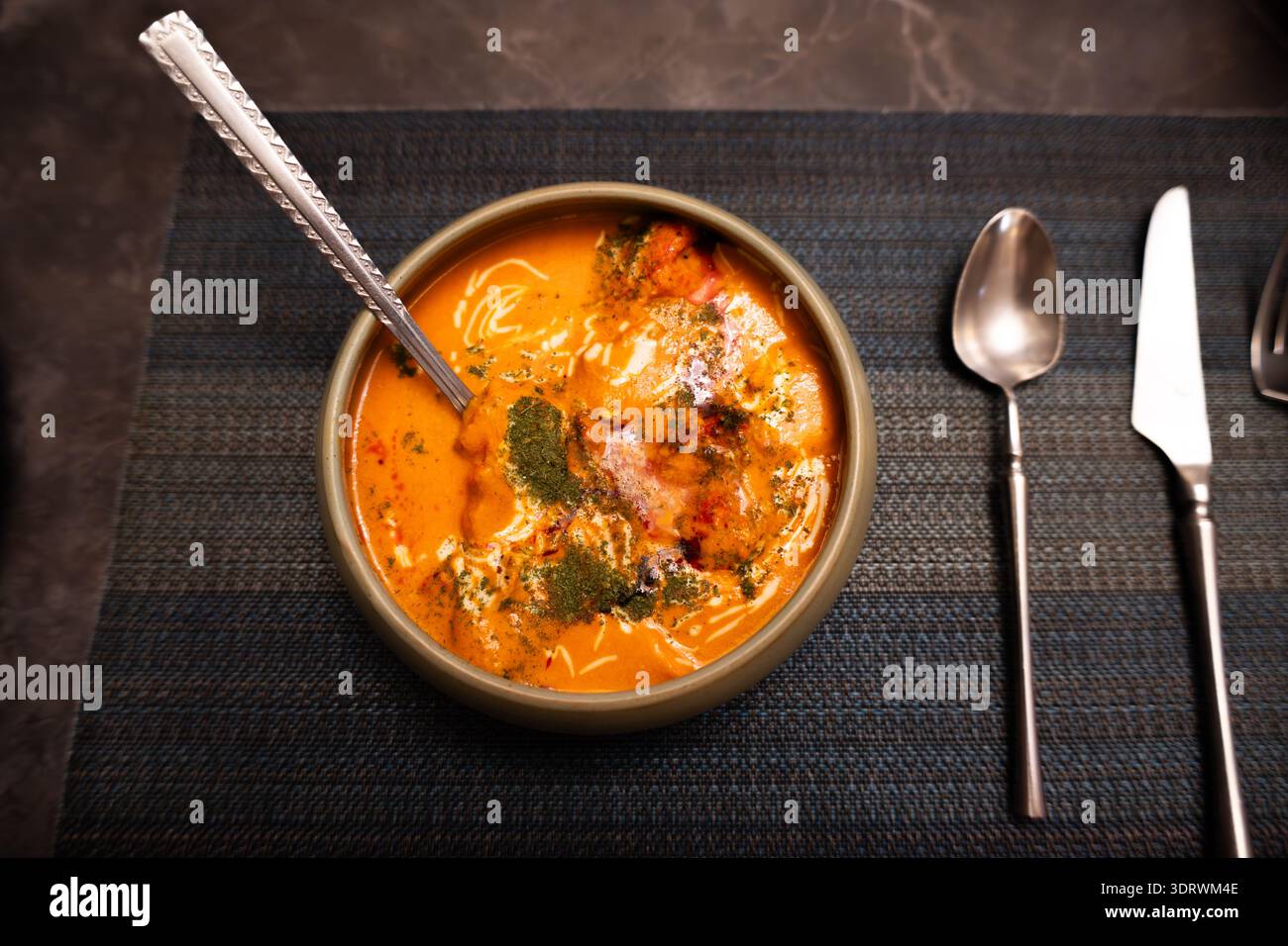 Zuppa turca di lenticchie in ciotola in ceramica con cucchiaio su tovaglia testurizzata scura, guarnita con erbe e yogurt Foto Stock