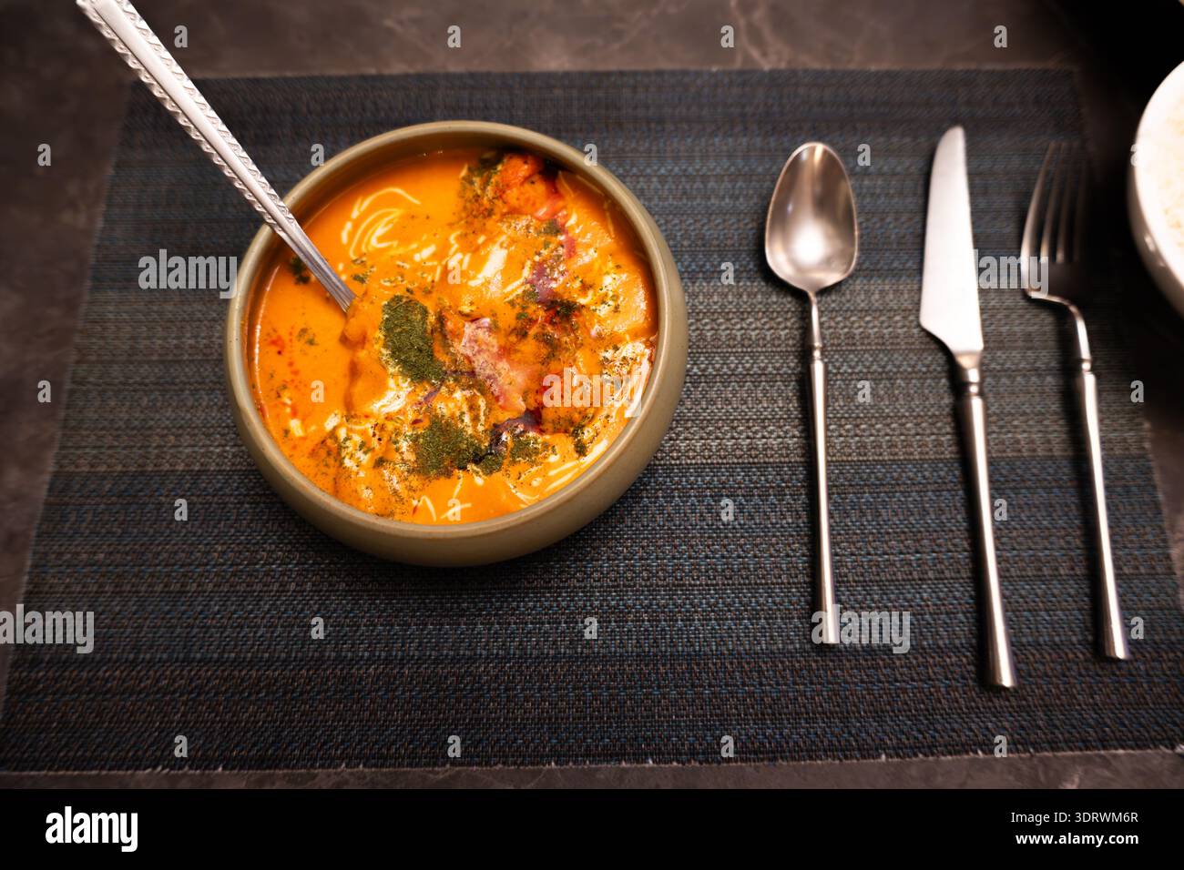 Zuppa indiana al curry in ciotola in ceramica con cucchiaio e posate su Placemat testurizzato scuro Foto Stock