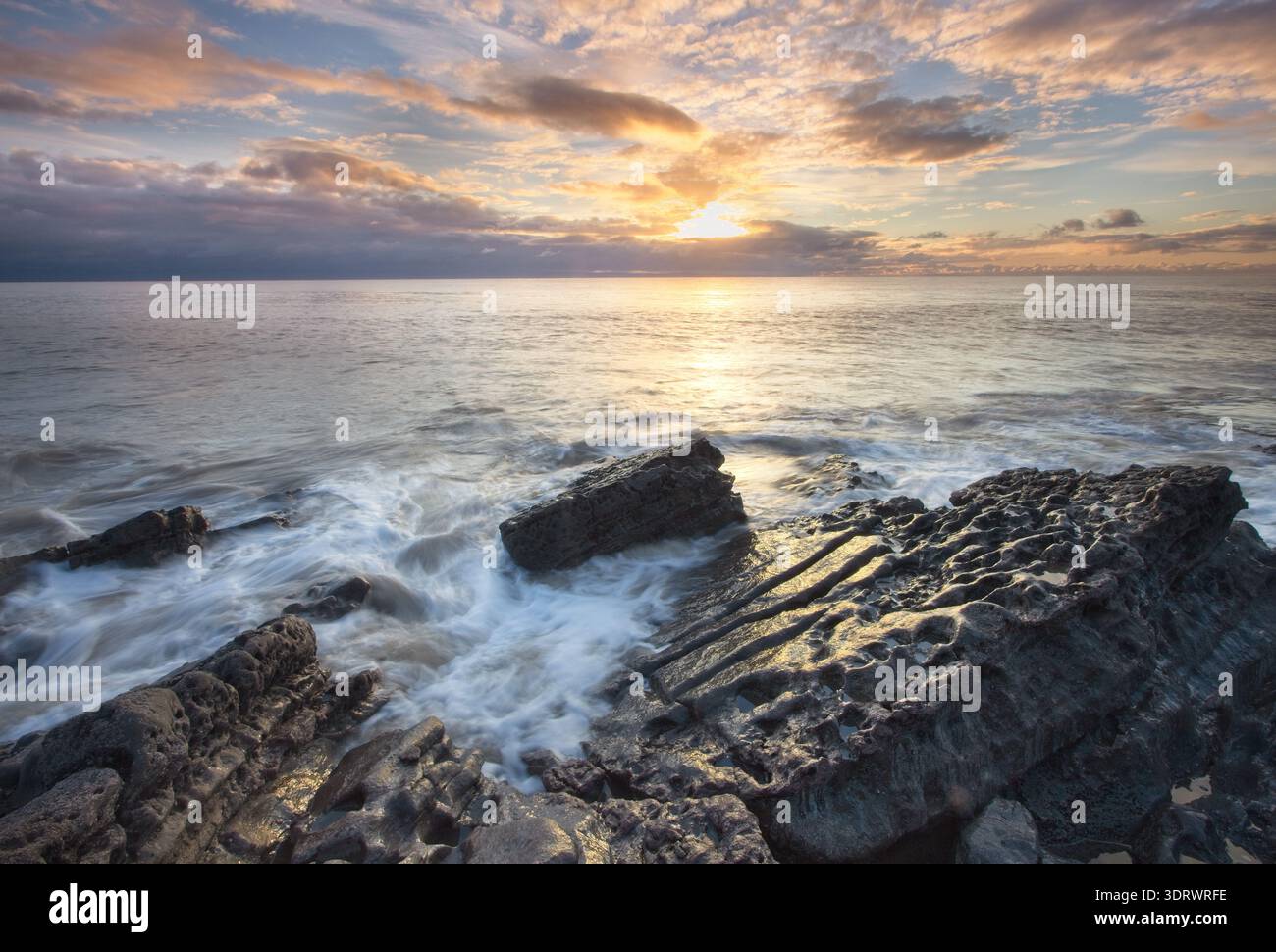 Costa rocciosa al tramonto con le onde che scivolano su sporgenze di pietra calcarea strutturata sulla Welsh Heritage Coast. Foto Stock