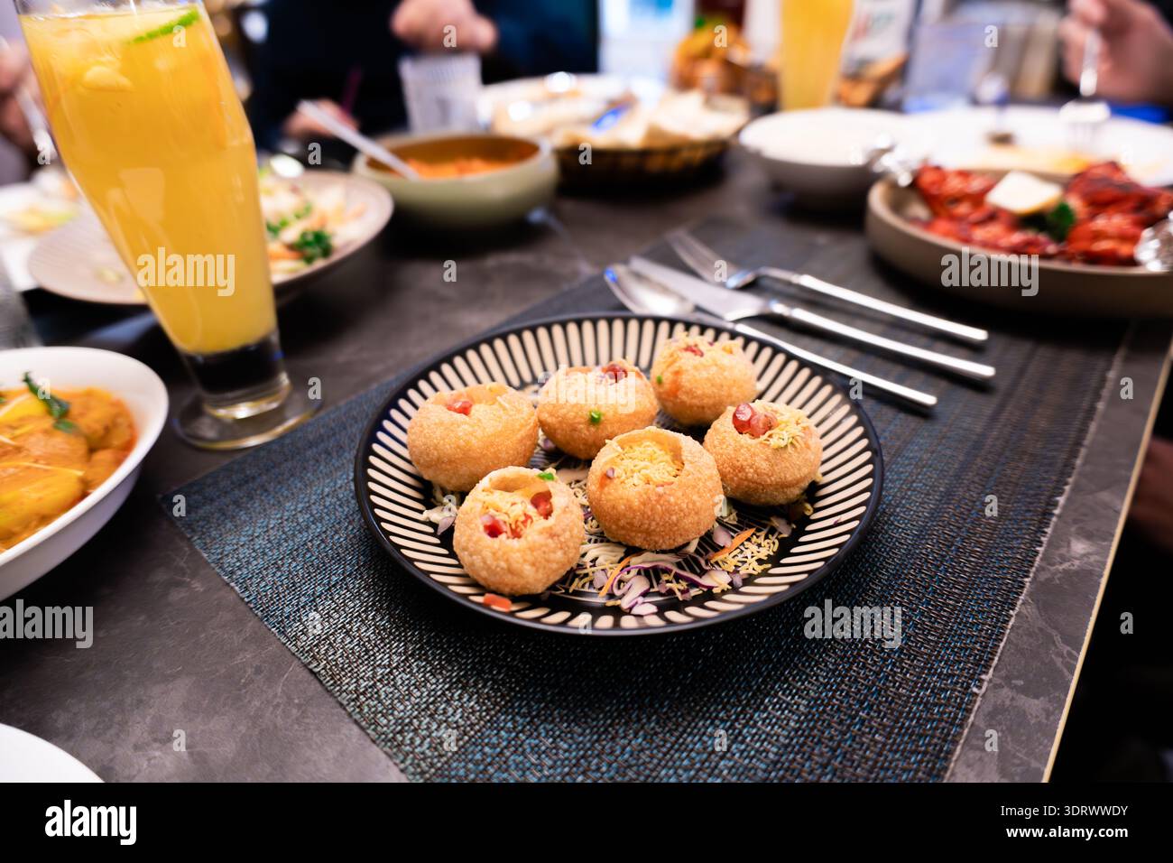 Spuntini indiani Pani Puri su piatto a motivi con bevande e contorni al tavolo del ristorante Foto Stock