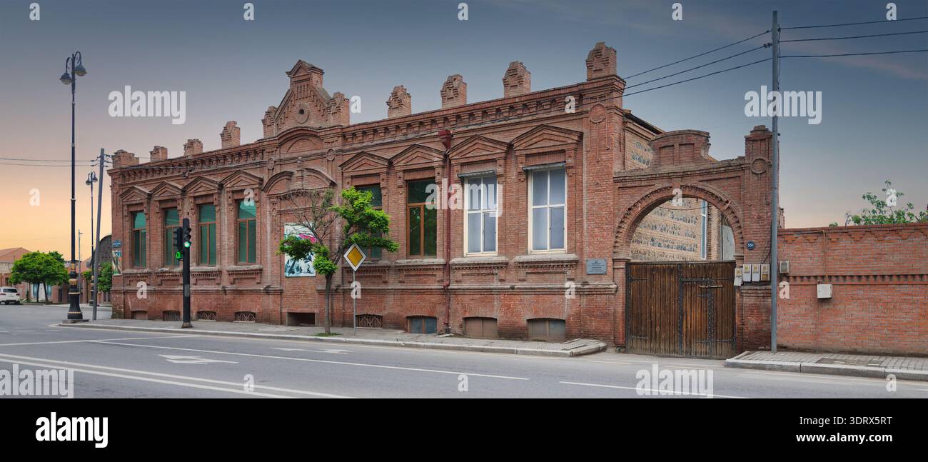 Ganja, Azerbaigian - 13 maggio 2024: Storico edificio in mattoni rossi con facciata ornata e ingresso ad arco, con un cartello Yasayis evi, in una strada tranquilla sotto un cielo limpido Foto Stock