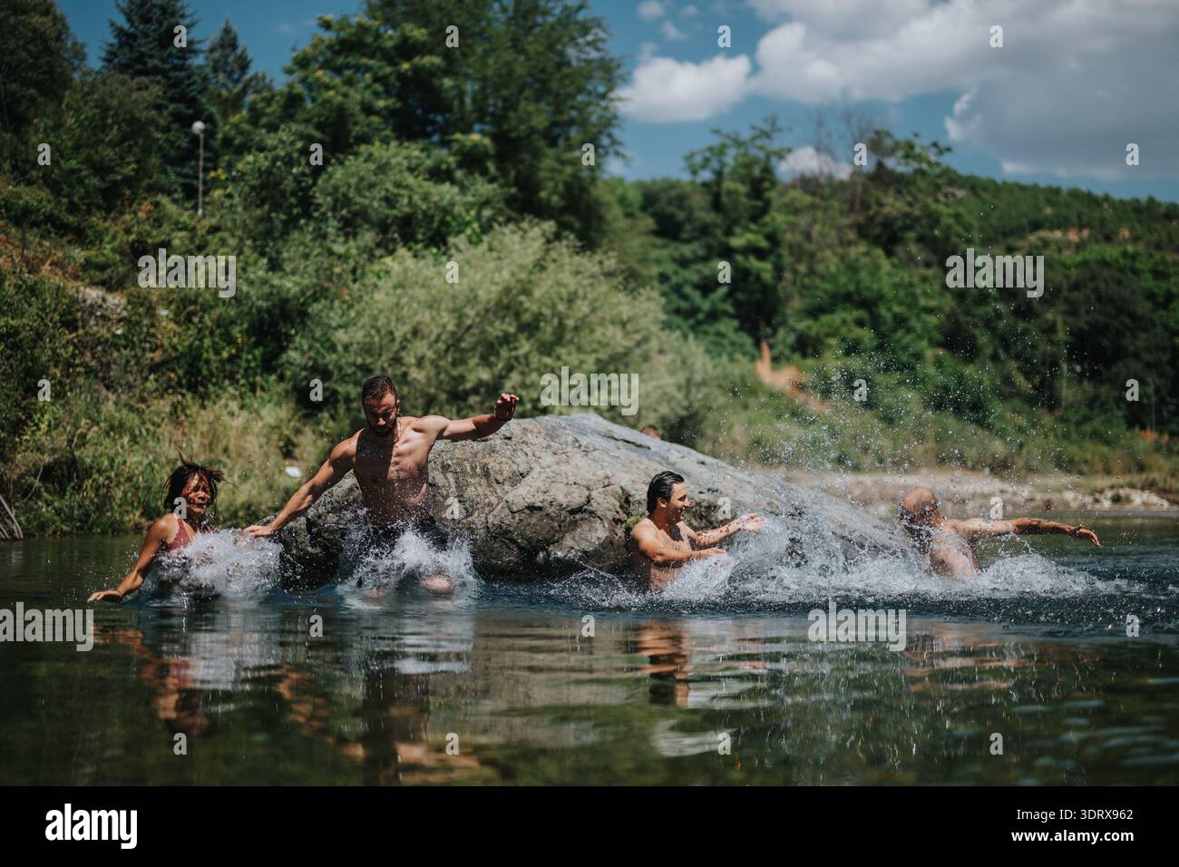Gli amici si divertono con un divertente tuffo sul fiume e si tuffano da una roccia in una soleggiata giornata estiva Foto Stock
