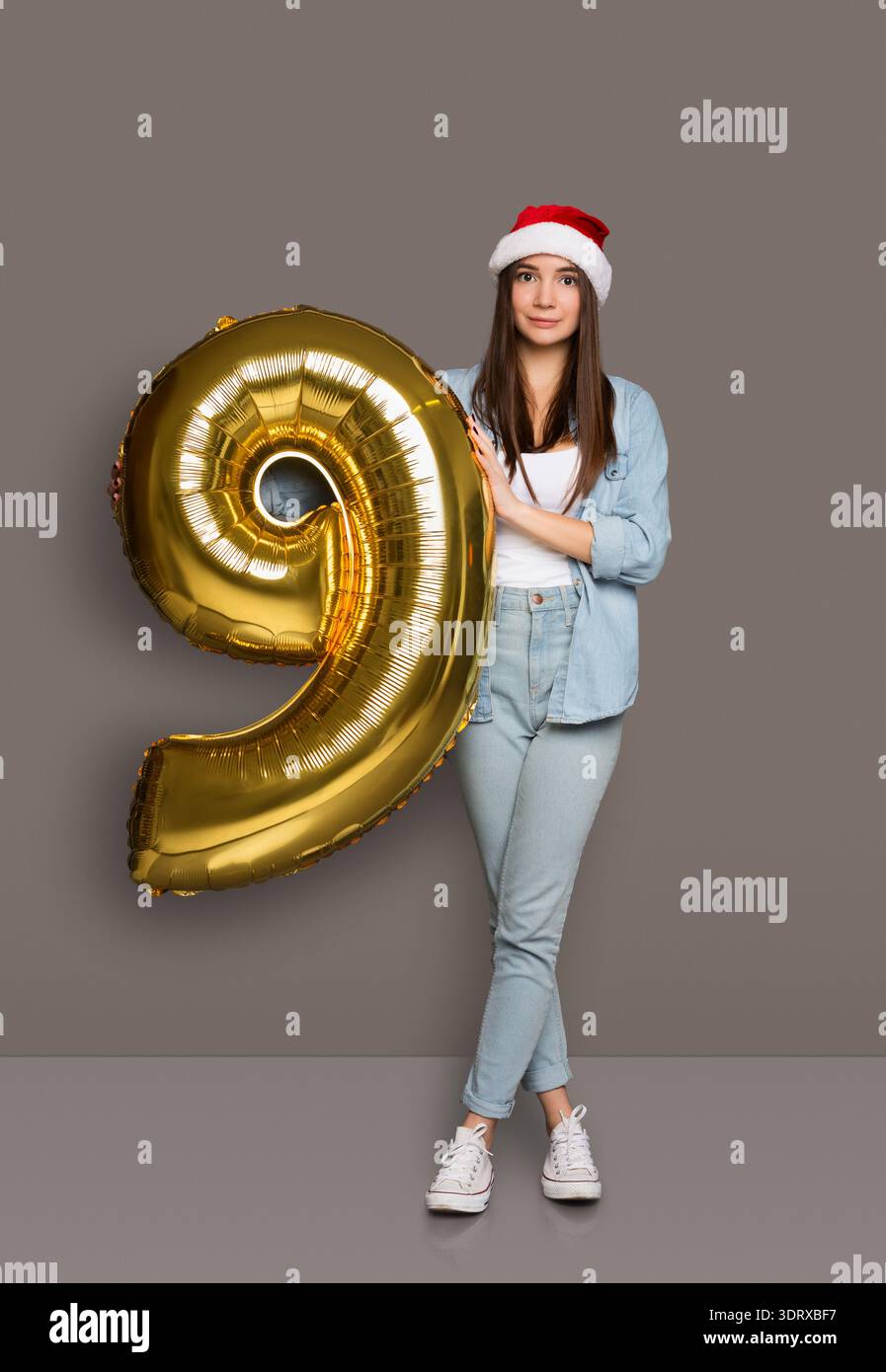 Young Woman detiene un grande pallone numero 9 d'oro per la celebrazione durante le festività Foto Stock