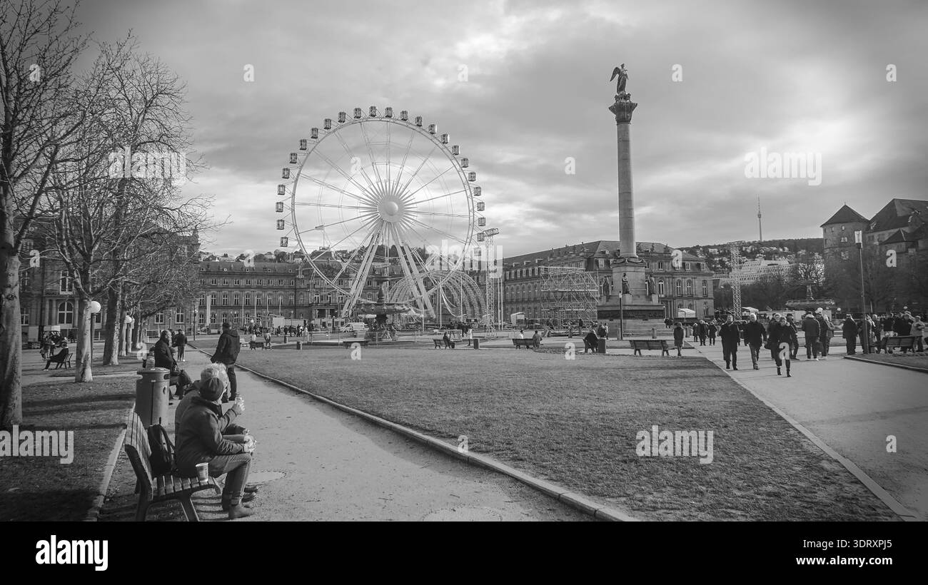 Ruota panoramica in un parco con visitatori, incorniciato da edifici storici sotto un cielo nuvoloso, creando una tranquilla scena urbana di svago. Foto Stock