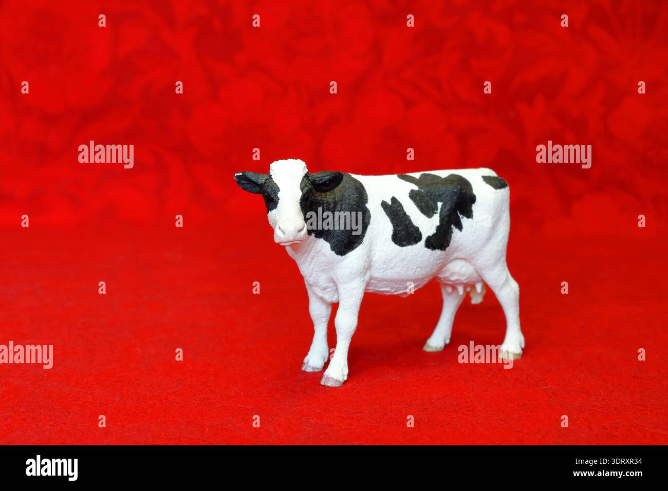 Mucca bianca e nera. Giocattolo di plastica con sfondo rosso. Foto Stock