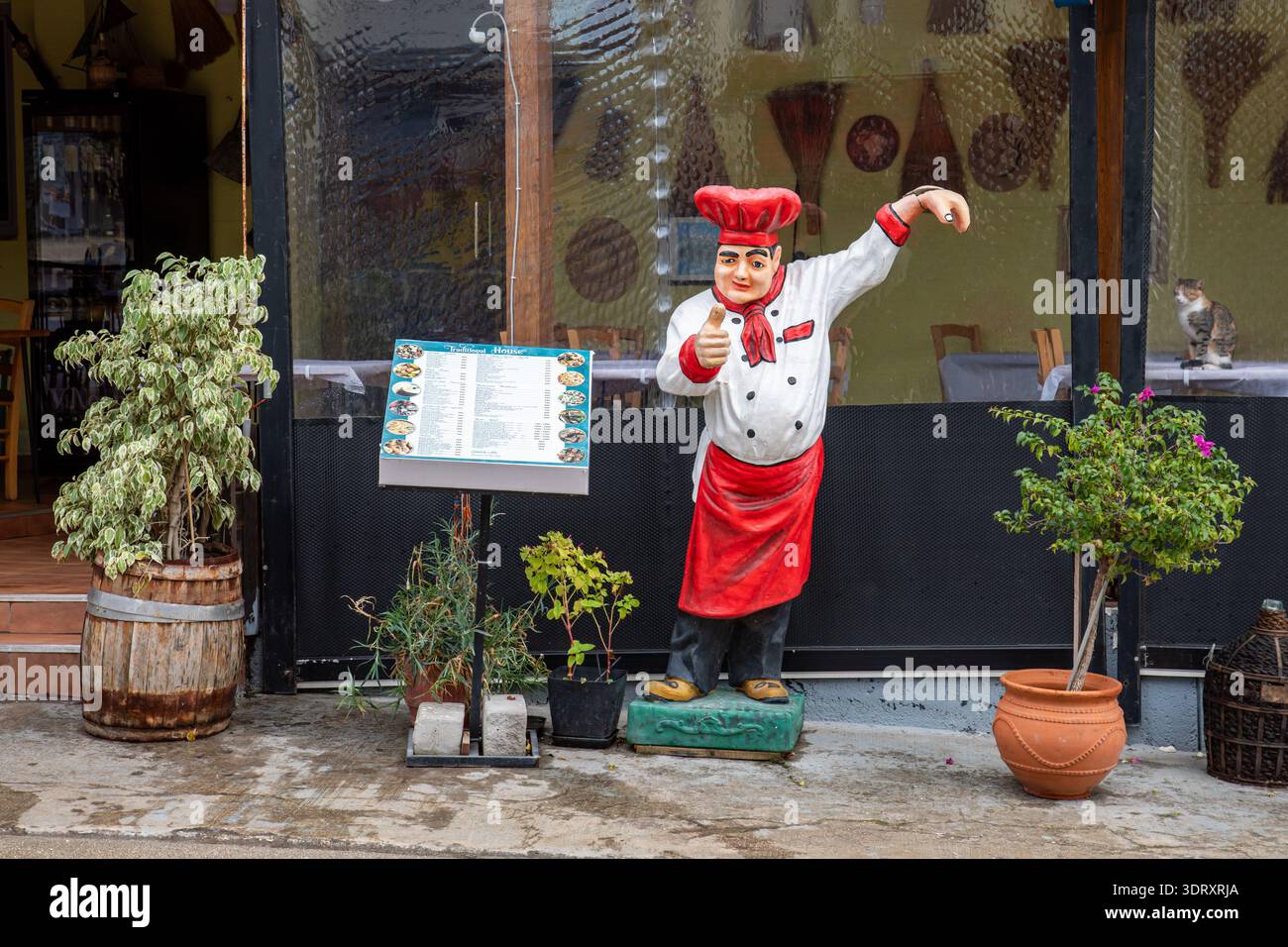 Statua promozionale del cuoco accanto al tabellone del menu all'aperto di fronte a un ristorante chiuso a Ksamil, Albania Foto Stock