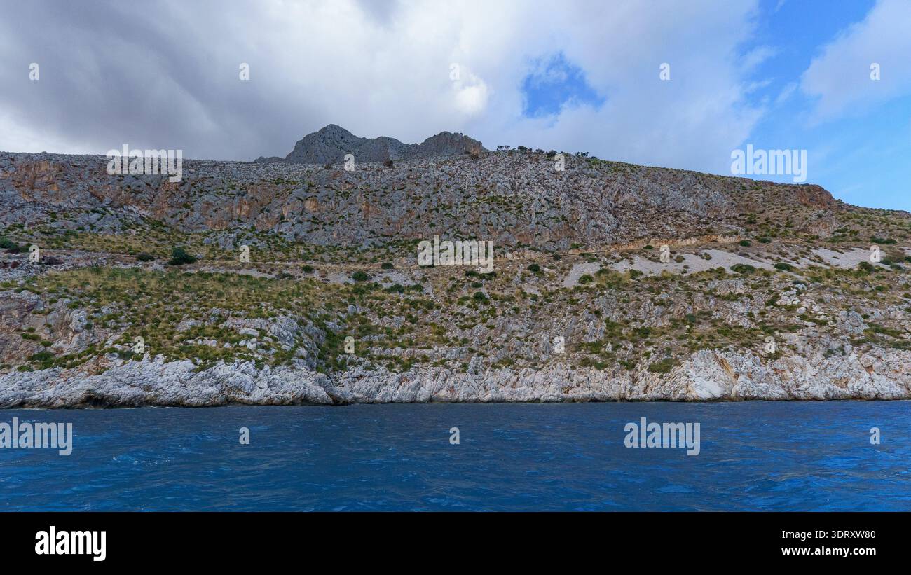 Una spettacolare vista ad alto angolo che cattura la bellezza selvaggia e aspra della costa siciliana, dove una ripida collina rocciosa scende bruscamente al mare, enfasi Foto Stock