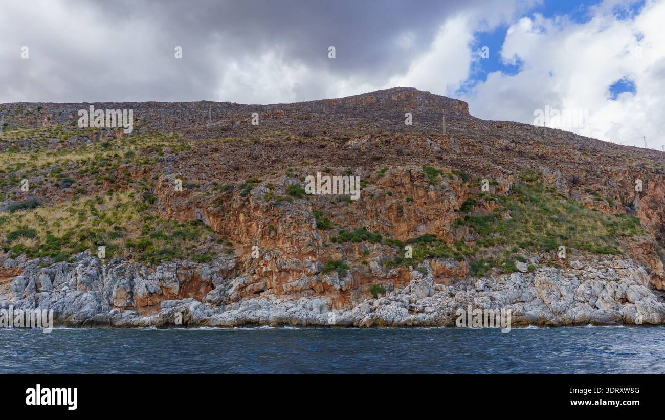 Una spettacolare vista ad alto angolo che cattura la bellezza selvaggia e aspra della costa siciliana, dove una ripida collina rocciosa scende bruscamente al mare, enfasi Foto Stock